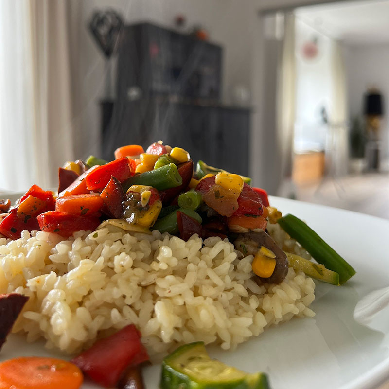 Plato de arroz con veruras encima de mesa con fondo de un hogar